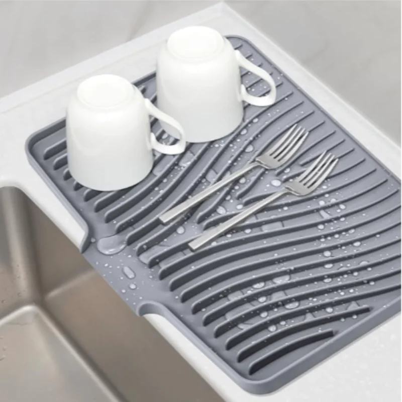 Silicone dish drying mat with built-in drain beside a sink
